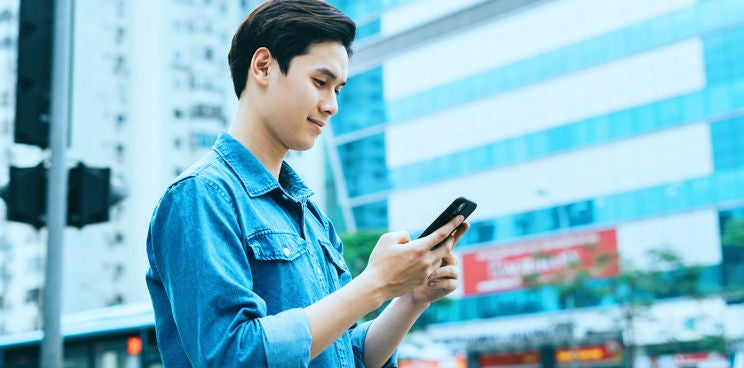 A man checking his mobile phone outside with office buildings in the background.