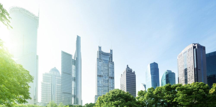 Low angle shot of skyscrapers with trees and view of the blue sky.