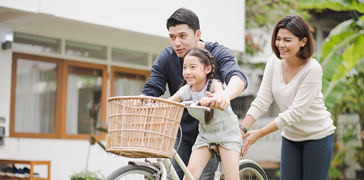A young daughter being taught how to ride a bike by her parents