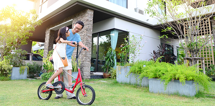 A father teaching his daughter how to ride a bike in the yard of their new house